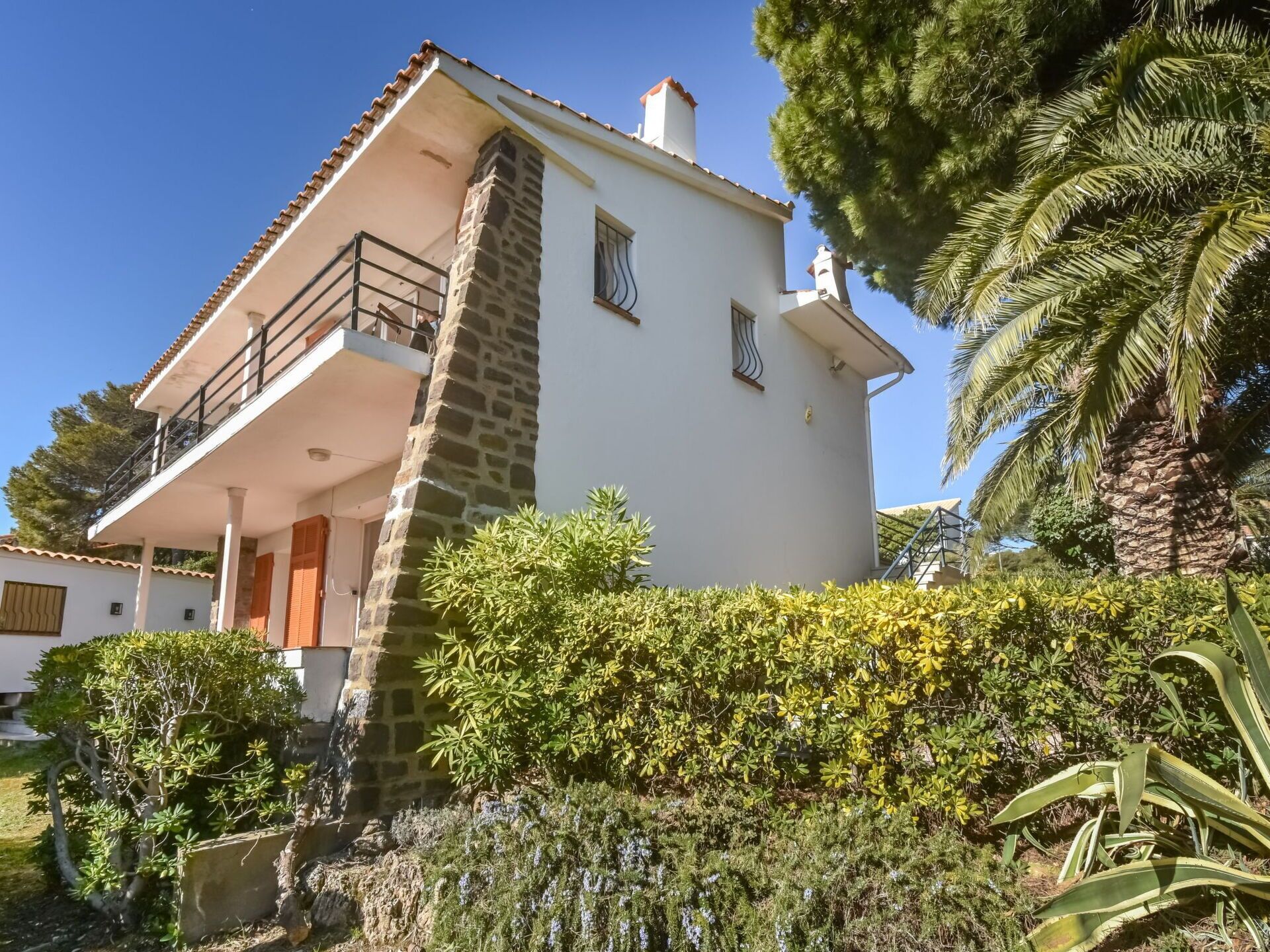 Una casa de dos pisos con balcón, pilar de piedra y abundante vegetación.