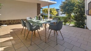 Eine Terrasse im Freien mit einem Esstisch, umgeben von Stühlen, und ein Balkon darüber.