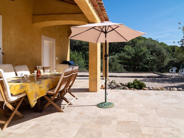 An outdoor dining area with a table set for four, a grill, and a patio umbrella.