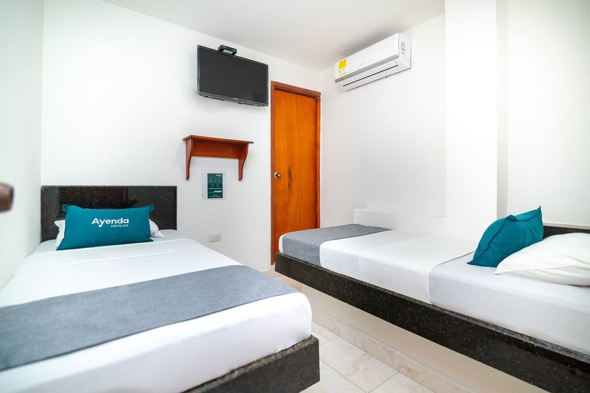 A hotel room with two beds, a TV, an air conditioner, and a wooden door.