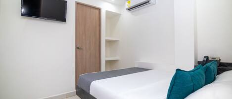 A bedroom with a bed, a TV mounted on the wall, and an air conditioning unit.