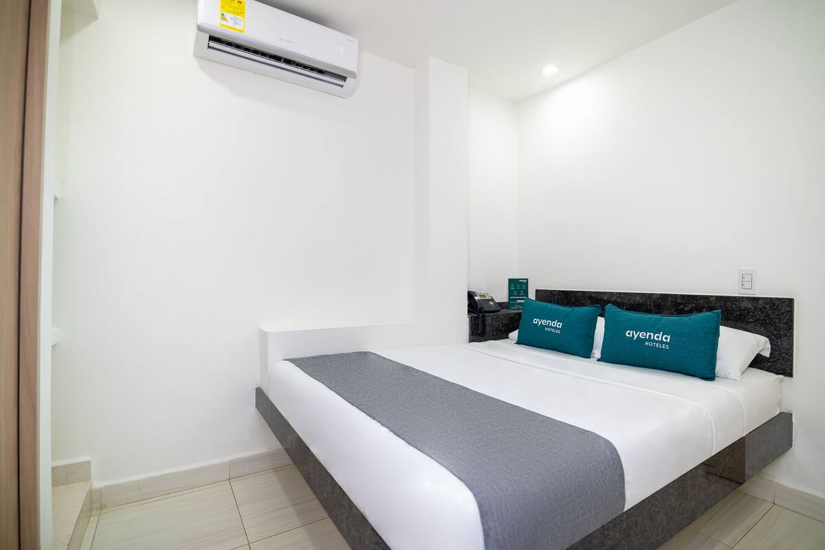 A hotel room with a bed, a nightstand, and an air conditioning unit.
