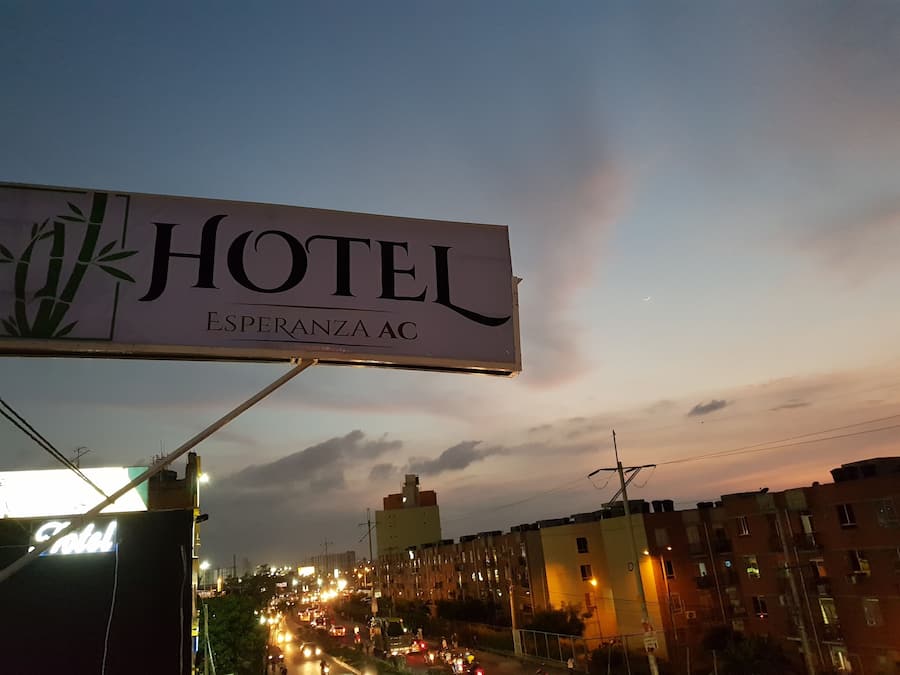 Letrero de hotel con el nombre "HOTEL ESPERANZA AC" y una vista parcial del área urbana circundante al anochecer.