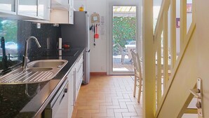 A modern kitchen with a sink, cabinets, and a refrigerator. There is a dining area with chairs and a table visible through an open door.