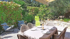 An outdoor dining area with a table set for two, surrounded by wicker chairs, under a striped awning.