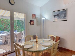 Un coin repas avec une table en verre, des chaises et un ensemble de vaisselle. Une porte donne accès à un espace extérieur aménagé avec des chaises et une table.