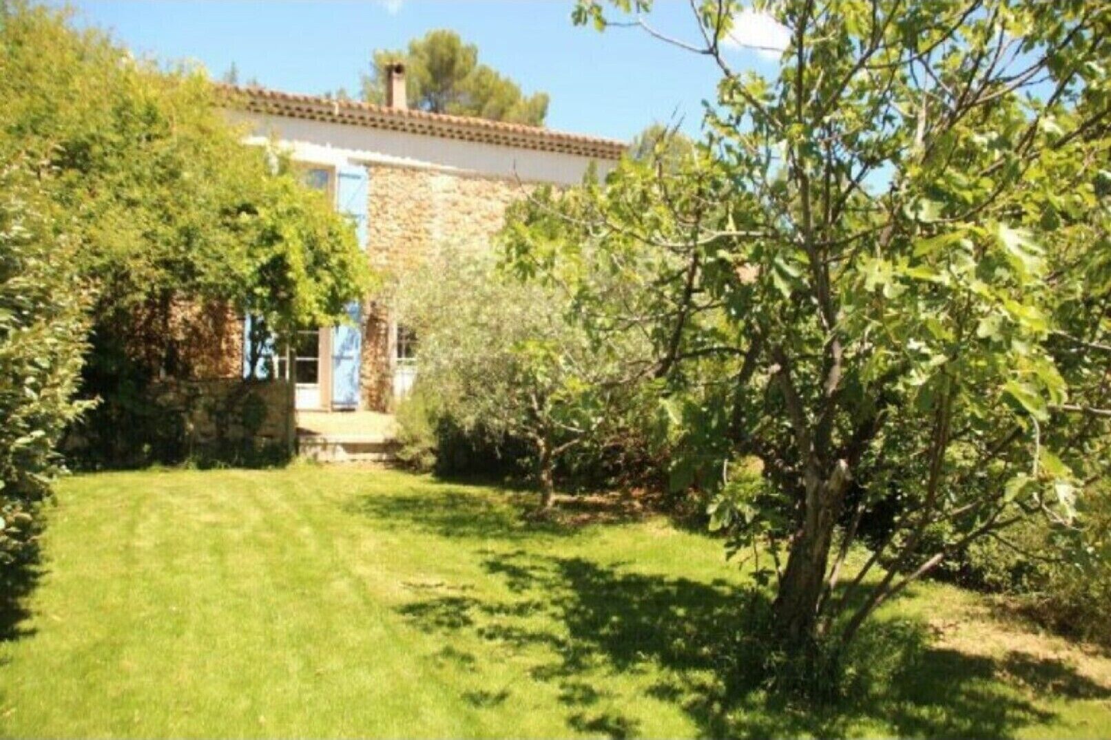 Une maison en pierre avec un toit de tuiles, entourée d’une pelouse bien entretenue et d’un feuillage dense.