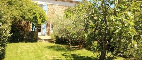 Une maison en pierre avec un toit de tuiles, entourée d’une pelouse bien entretenue et d’un feuillage dense.