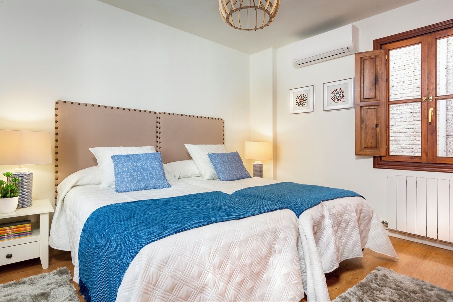 A bedroom with a large bed, a bedside table with a lamp, a potted plant, and a window with a view.