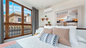 Ett hotellrum med en säng, ett fönster med utsikt över byggnader, en väggmonterad luftkonditioneringsanläggning och en tavla.