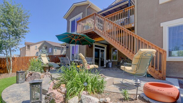 A backyard with a patio, outdoor furniture, a fire pit, and a staircase leading to a deck.