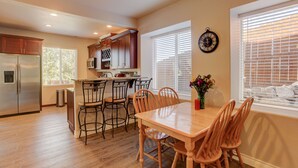 A kitchen with wooden cabinets, a stainless steel refrigerator, and a dining area with a wooden table and chairs.
