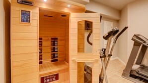 A sauna with wooden walls, a control panel, and a mirror. Adjacent to the sauna is a treadmill.