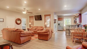 A spacious living room with a large sectional sofa, a dining area with wooden chairs, a kitchen with a refrigerator and microwave, and a ceiling fan.