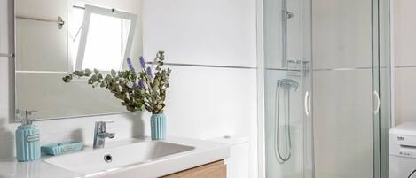 Un baño moderno con un lavabo blanco, tocador de madera, cabina de ducha de vidrio y baldosas de suelo estampadas.