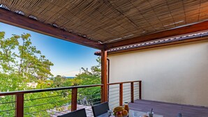 Un espace de restauration en plein air avec une table dressée pour deux personnes, entouré de chaises en osier, donnant sur un jardin luxuriant et un ciel bleu azur.
