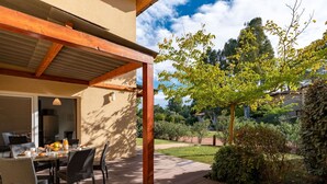 An outdoor patio with a wooden deck, a table with chairs, and a view of a garden with trees and shrubs. - Cosy apartment for 6 people with WIFI, pool, A/C, TV, terrace and pets allowed (Porto-vecchio)