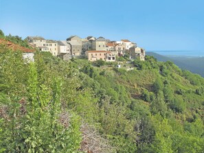 Un pueblo en la ladera con edificios de piedra tradicionales, abundante vegetación y una vista despejada del mar.