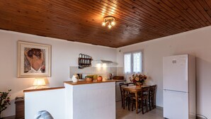 A compact kitchen with a wooden ceiling, a central island, a dining table with chairs, and a refrigerator.