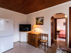 Una cocina compacta con refrigerador, un mueble de madera, televisión y una silla.