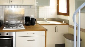 A compact kitchen with a gas stove, coffee maker, and a sink. There is a small oven and a cabinet with drawers.