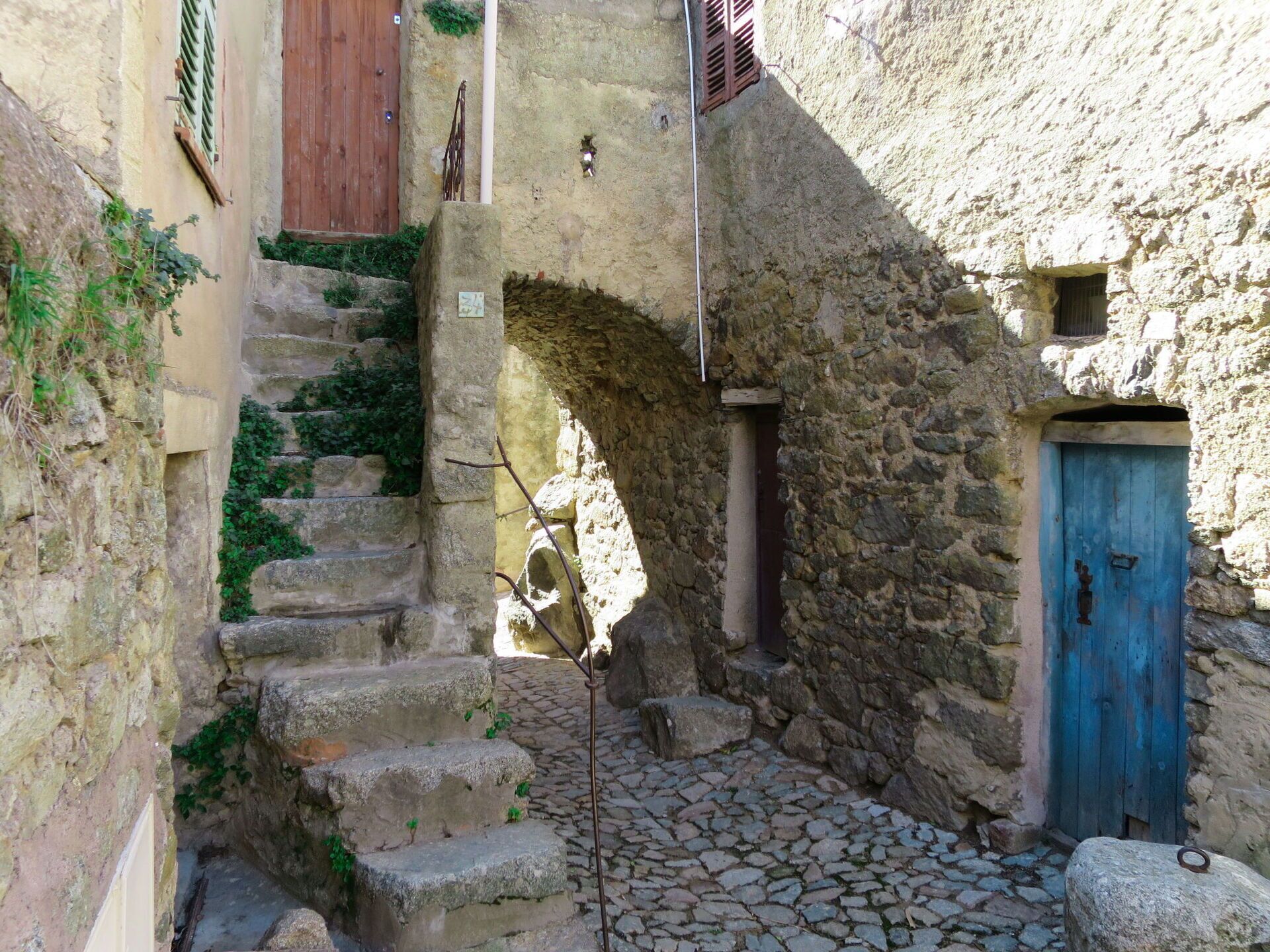 A narrow stone staircase leading up to a wooden door, surrounded by stone walls and a cobblestone path.