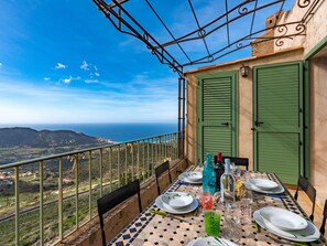 A dining table set on a balcony with a view of the sea and hills.