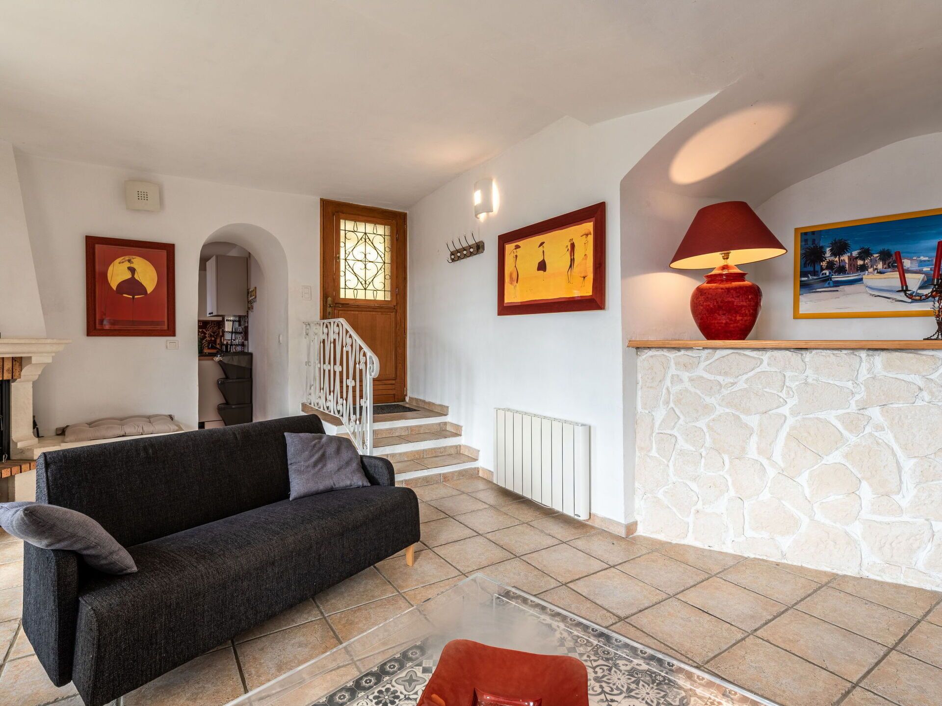 A living room with a sofa, a glass coffee table, a red lamp, a stone fireplace, and a staircase leading to another room.