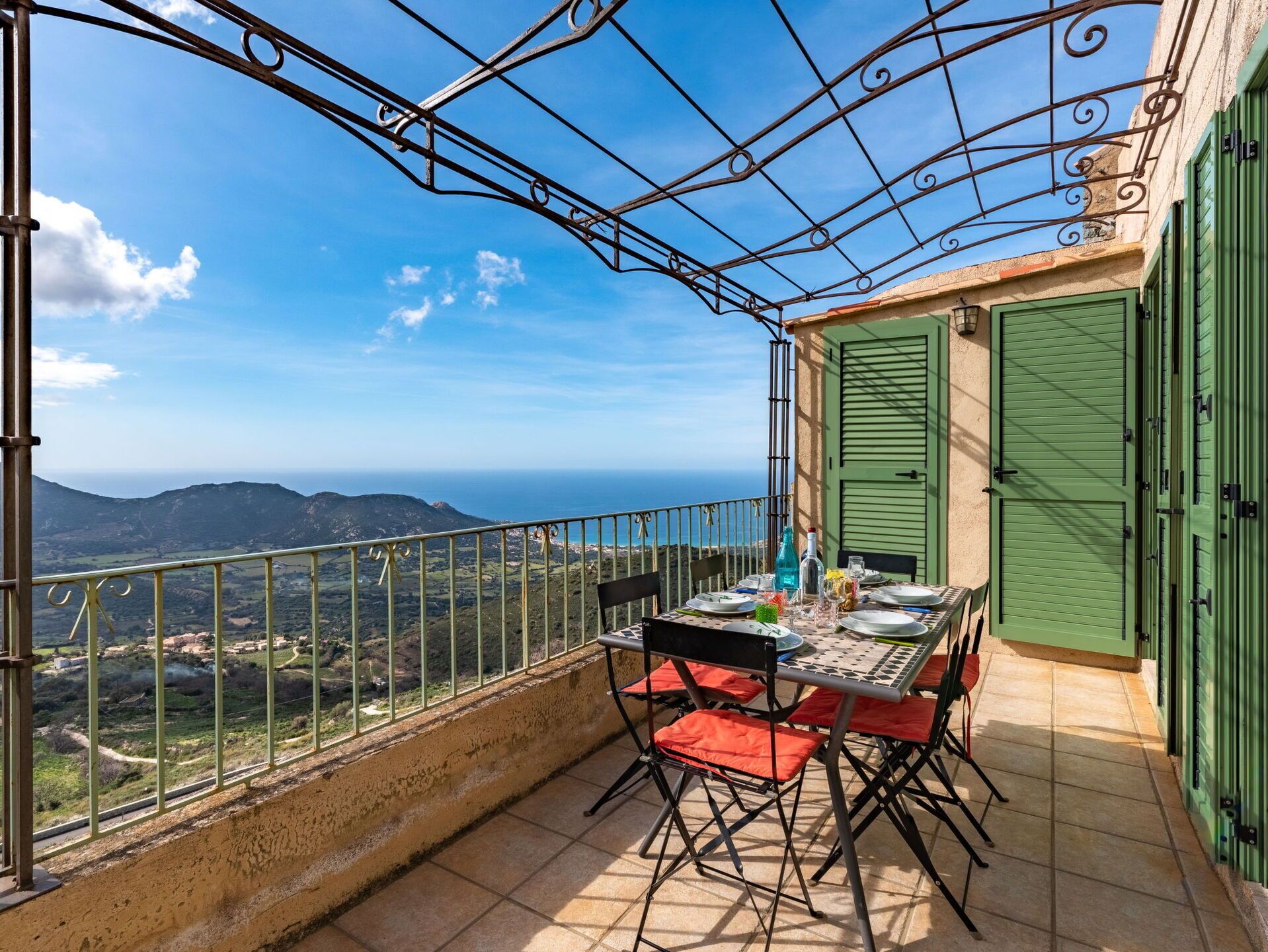 A balcony with a table set for two, overlooking a scenic landscape with mountains and the sea.