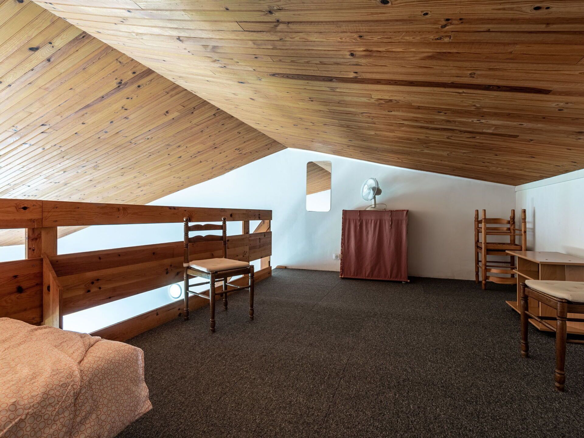 A cozy attic room with a sloped ceiling, wooden furniture, and a small table with a fan.