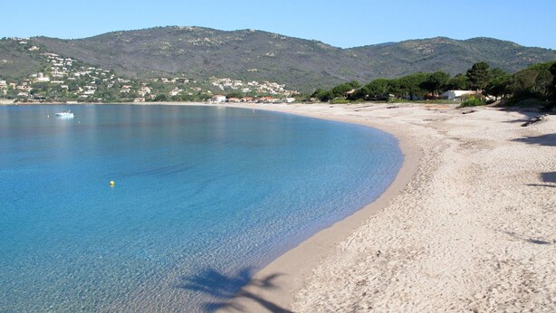A beach with clear blue water, a sandy shore, and a backdrop of hills with buildings. - Cosy apartment in villa for 6 guests with TV, terrace and pets allowed (Coggia)