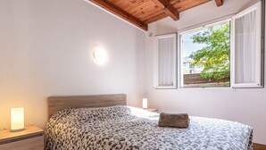 A bedroom with a wooden headboard, a patterned bedspread, a bedside lamp, and a window with a view of greenery. - Cosy apartment in villa for 6 guests with TV, terrace and pets allowed (Coggia)
