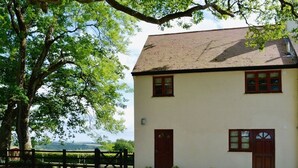 Un bâtiment à deux étages, à l’extérieur blanc et aux bordures marron, doté de deux portes et de deux fenêtres, entouré d’une allée en gravier et d’une clôture en bois.