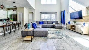 A spacious living area with a sectional sofa, a dining table with chairs, a kitchen area, and a TV mounted on the wall. - Champion Gate Brand New Home with Private pool and  game room (Davenport)