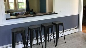 Una cocina con barra integrada, tres taburetes y un espejo grande sobre la encimera.