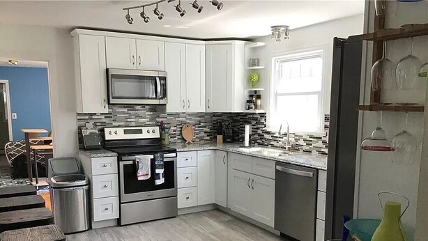 Una cocina moderna con armarios blancos, microondas, estufa y lavavajillas. Hay un comedor con mesa y sillas.