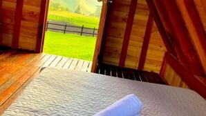 Een gezellig slaapkamer op zolder met een houten plafond, een bed met sprei en uitzicht op een groen veld door een geopende deur.