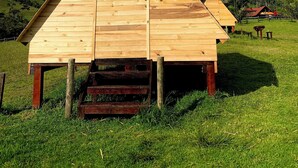 Een piramidevormige houten constructie met een trap die erheen leidt, gelegen in een grasveld met bergen op de achtergrond.