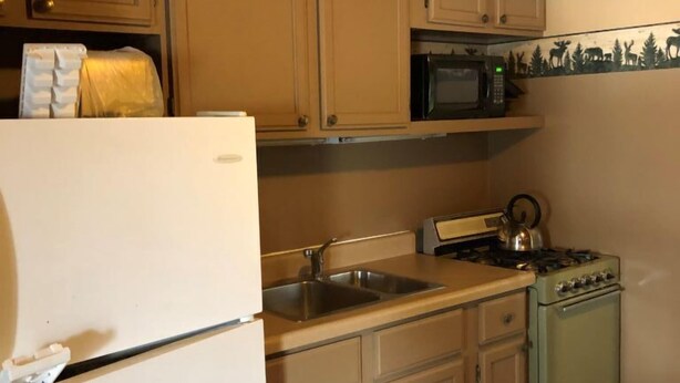 A kitchen with wooden cabinets, a white refrigerator, a microwave, a stove, and a sink. - Lakeside Cottage - Finch (Hawks)