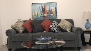 A living room with a grey sofa, a glass coffee table, and a patterned rug.