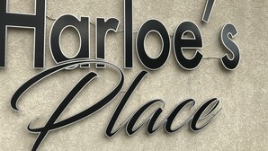 A sign with the text "Harloe's Place" in a stylized font against a textured wall.