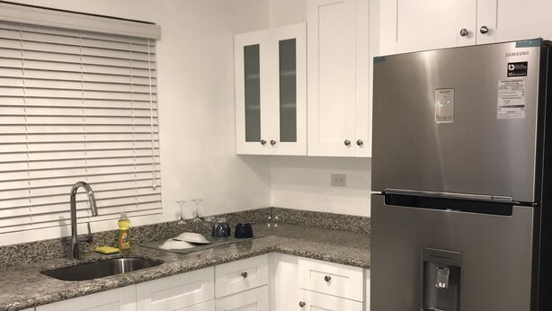 A modern kitchen with white cabinets, a stainless steel refrigerator, a granite countertop, and a built-in sink.