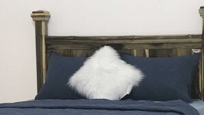 A bed with a wooden frame, dark blue bedding, and a white fluffy pillow.