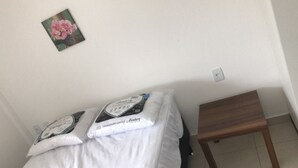 A bedroom with a bed, pillows, a small wooden table, and a wall-mounted light switch.