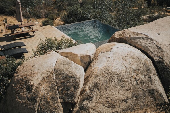 A pool with a wooden deck, surrounded by large rocks and vegetation.