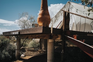 A rustic outdoor setting with a wooden structure, a large clay pot, and a tent.