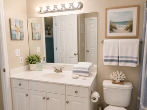 A bathroom with a sink, mirror, lights, towels, and a framed picture.