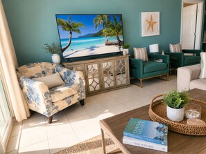 A living room with a TV, teal sofas, a floral armchair, a coffee table with books, and a starfish decoration.
