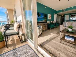 A living room with a view of the ocean, a balcony with outdoor furniture, and a kitchen area.