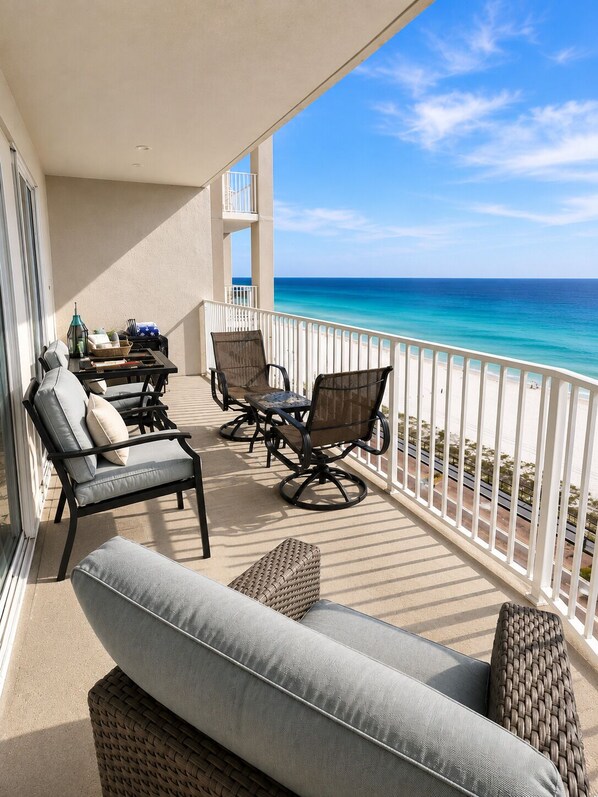 A balcony with a sofa, chairs, and a table, overlooking a beach.